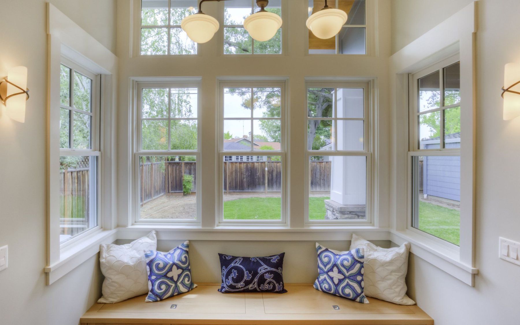 A sunlit window seat framed by white double-hung windows looking onto a garden