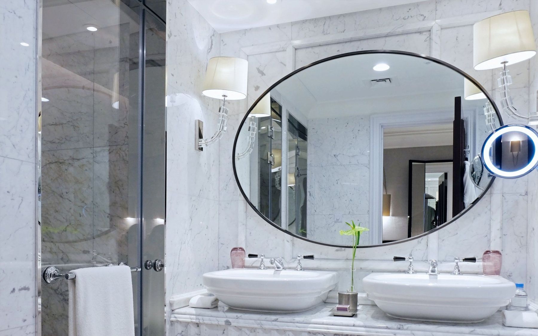 A large oval mirror mounted above twin basins in a marble bathroom