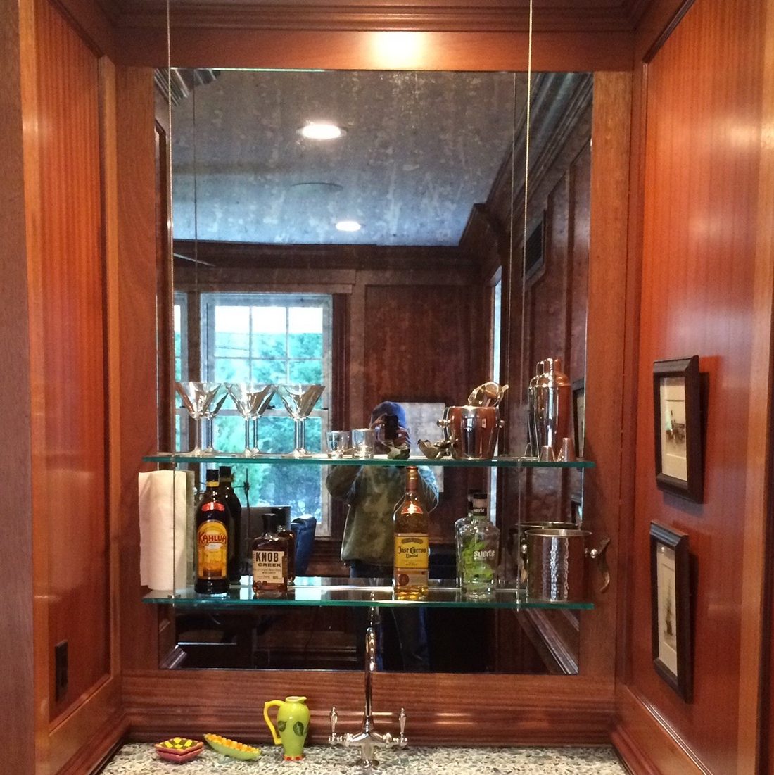 Custom cut wall mirror with floating glass shelves in a wood-panelled wet bar